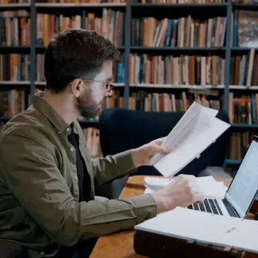 Intelektualac pred računalom i knjigom u knjižnici