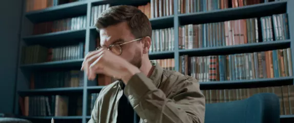 Muškarac s naočalama u knjižnici kako razmišlja