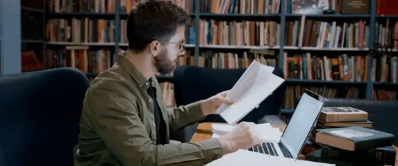 Intelektualac pred računalom i knjigom u knjižnici