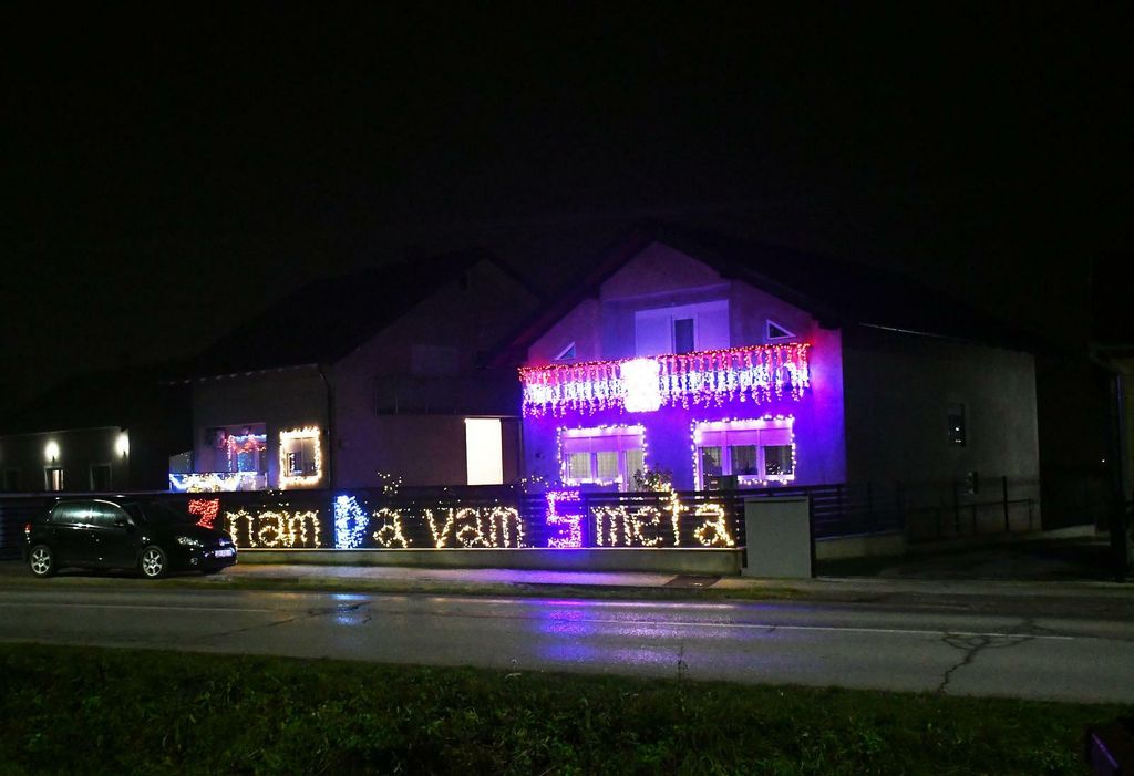 Kuća ukrašena tisućama lampica i osvijetljenom ogradom s natpisom