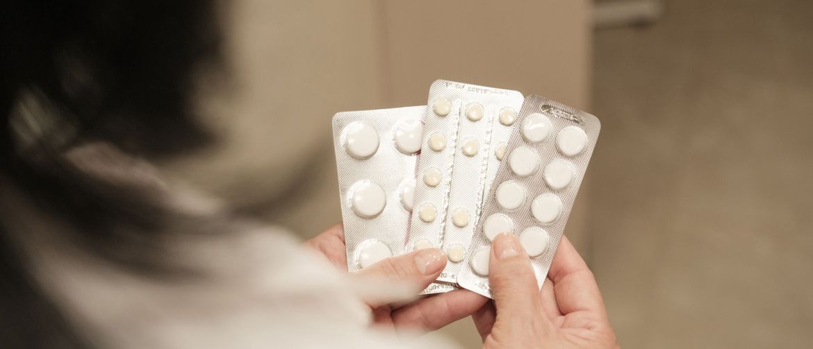 Žena srednjih godina koja drži nekoliko raznih tableta