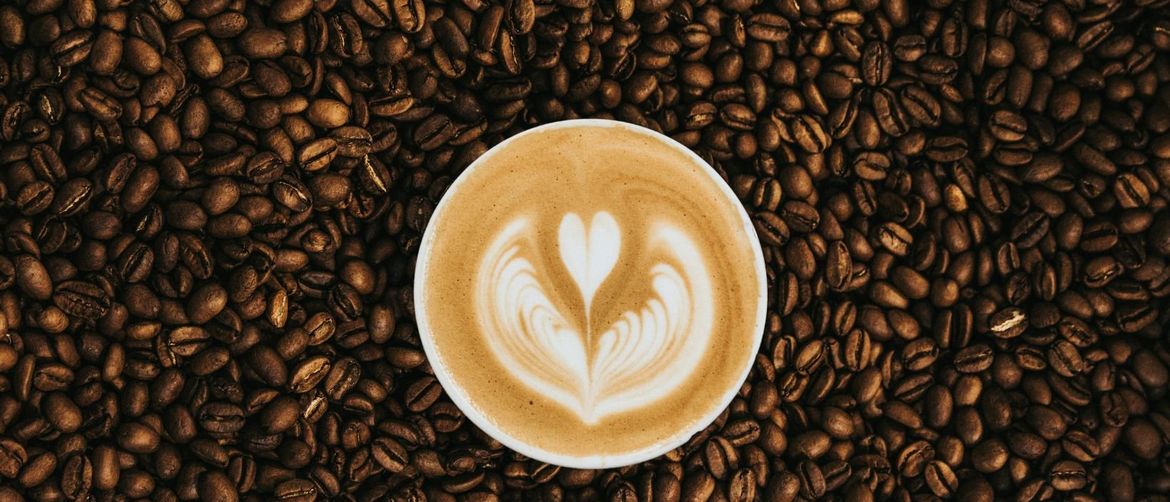 šalica skuhane kave na pozadini od zrna kave s dekoracijom od mlijeka u obliku srca