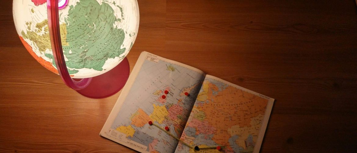 osoba sjedi nad atlasom i globus s označenim putovanjem na karti
