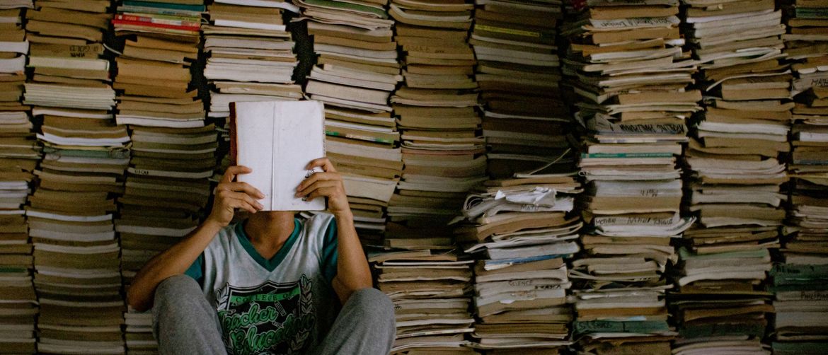 Muškarac kako sjedi ispred hrpe knjiga i čita