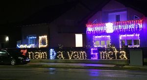 Kuća ukrašena tisućama lampica i osvijetljenom ogradom s natpisom