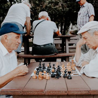 dva starija muškarca igraju šah na klupi u parku