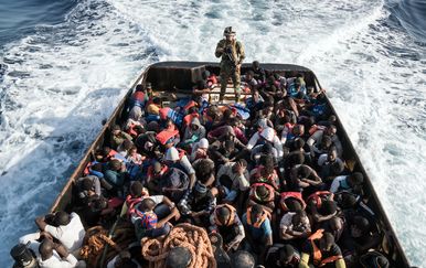 Pripadnik libijske obalne straže s presretnutim migrantima (Foto: AFP)