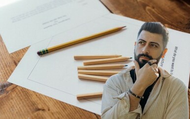 Lista papira s pitanjima i olovke na stolu uz muškarca koji razmišlja