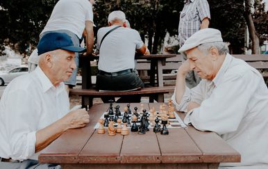 dva starija muškarca igraju šah na klupi u parku