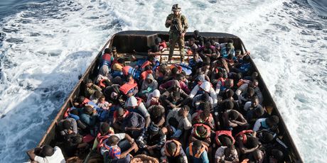 Pripadnik libijske obalne straže s presretnutim migrantima (Foto: AFP)