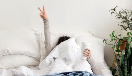 žena u krevetu prekrivena preko glave drži dva prsta u zraku
