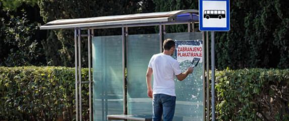 Muškarac koji uklanja natpis zabranjeno plakatiranje s autobusne stanice