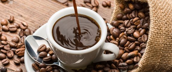 Točenje šalice kave i zrna kave na stolu oko šalice