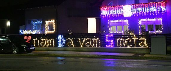 Kuća ukrašena tisućama lampica i osvijetljenom ogradom s natpisom