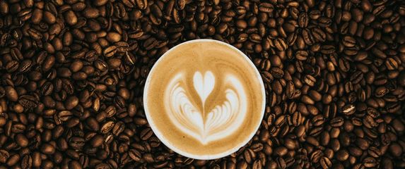 šalica skuhane kave na pozadini od zrna kave s dekoracijom od mlijeka u obliku srca