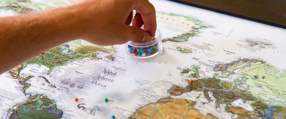stol s kartom svijeta i rukom koja postavlja oznake o lokacijama