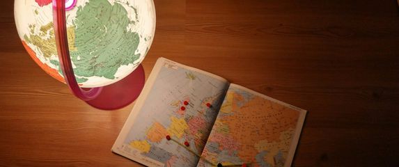 osoba sjedi nad atlasom i globus s označenim putovanjem na karti