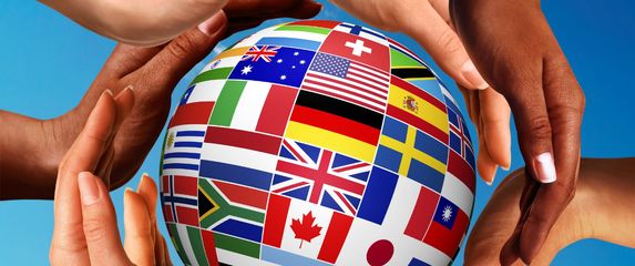 ruke koje okružuju globus na kojem su zastave nekih zemalja svijeta