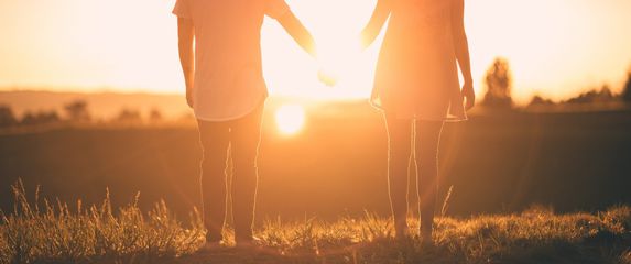 mladi par odlazi u zalazak sunca u prirodi držeći se za ruke