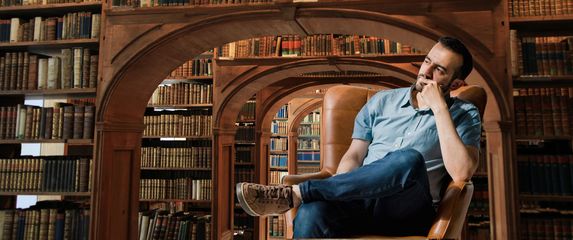 Knjižnica i muškarac u fotelji koji razmišlja