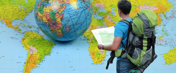 Muškarac s ruksakom i kartom ispred karte svijeta i globusa