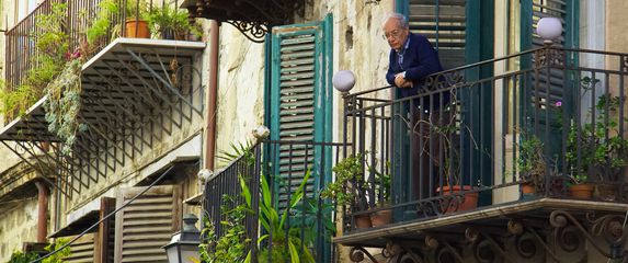 starac stoji na balkonu punom bilja