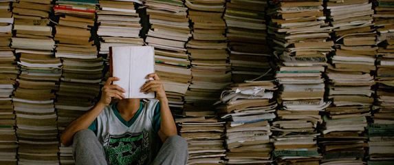 Muškarac kako sjedi ispred hrpe knjiga i čita