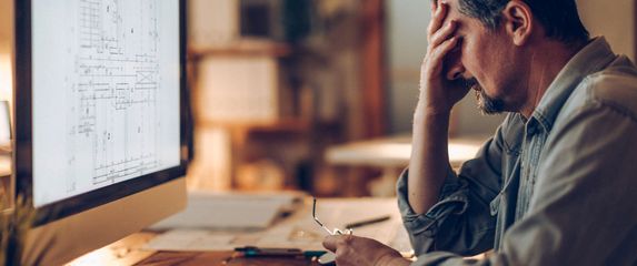 Muškarac koji razmišlja pred računalom i drži se za glavu