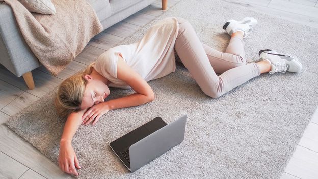 Umorna žena leži u sportskoj odjeći uz upaljeni laptop