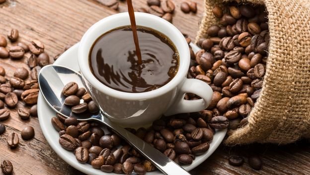 Točenje šalice kave i zrna kave na stolu oko šalice