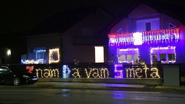 Kuća ukrašena tisućama lampica i osvijetljenom ogradom s natpisom