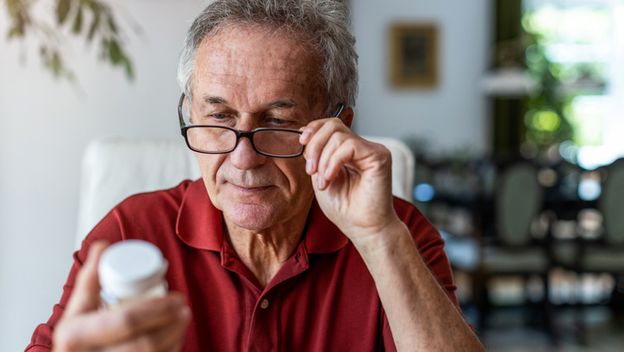 Stariji muškarac proučava kutiju s tabletama, ilustracija