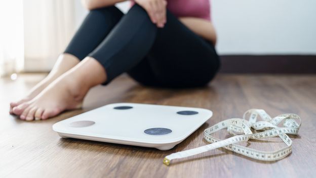 Pretila žena sjedi pored vage, ilustracija