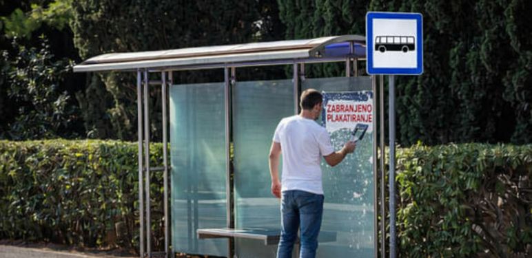 Muškarac koji uklanja natpis zabranjeno plakatiranje s autobusne stanice
