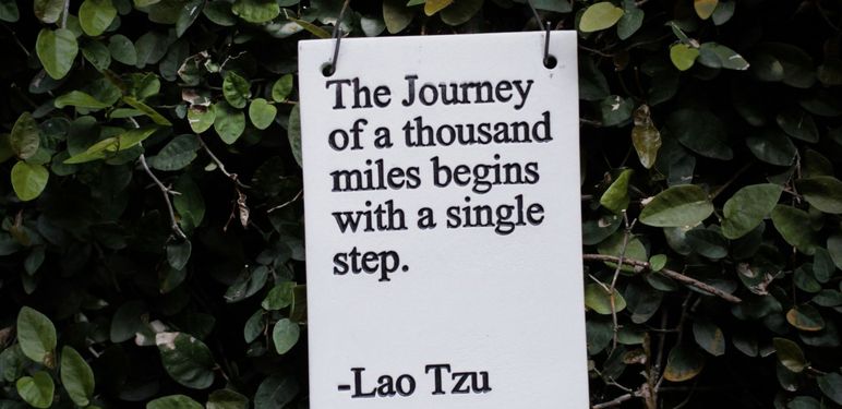 citat laoa tzua kako visi na pozadini od lišća na kojem piše da putovanje započinje jednim korakom