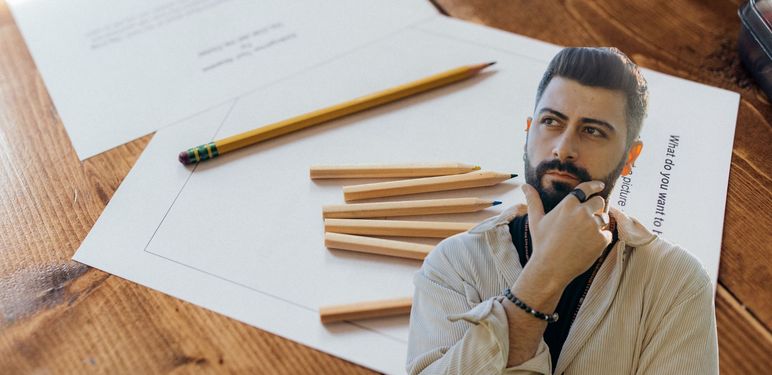 Lista papira s pitanjima i olovke na stolu uz muškarca koji razmišlja