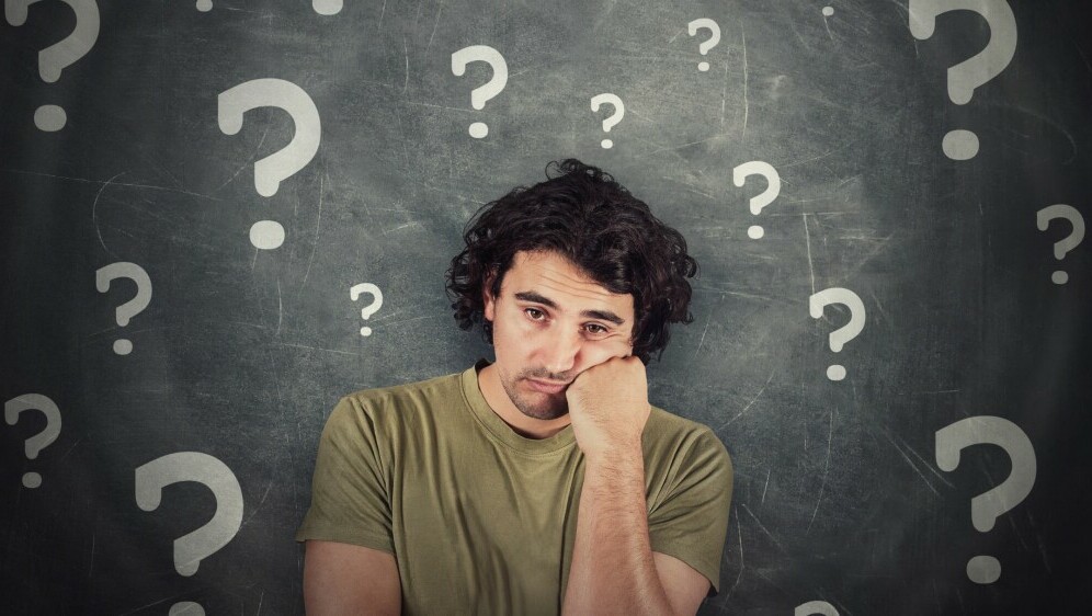 Muškarac koji razmišlja okružen upitnicima
