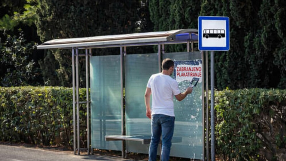 Muškarac koji uklanja natpis zabranjeno plakatiranje s autobusne stanice