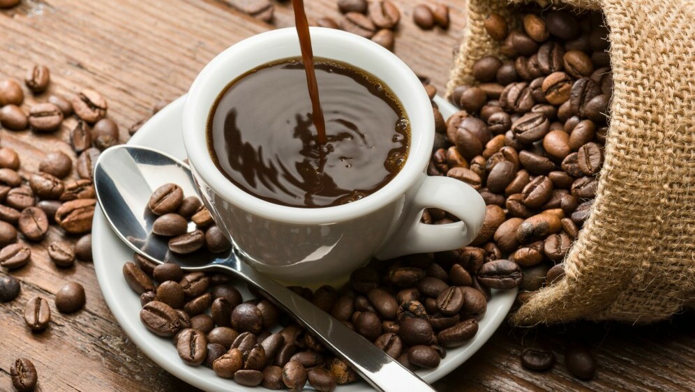 Točenje šalice kave i zrna kave na stolu oko šalice