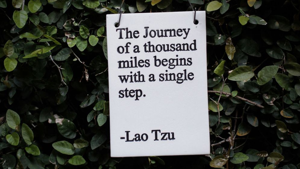 citat laoa tzua kako visi na pozadini od lišća na kojem piše da putovanje započinje jednim korakom