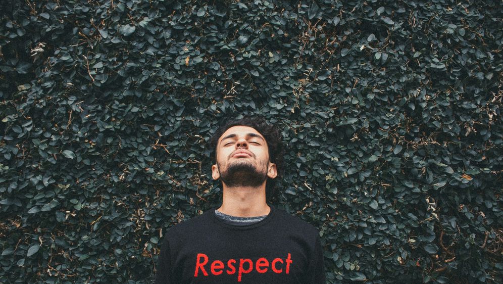 Muškarac pozira ispred grmlja s majicom na kojoj piše respect (poštovanje)