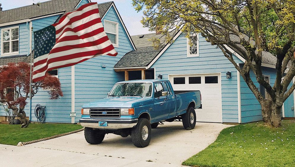 Automobil sparkiran na prilazu ispred kuće i američka zastava koji simboliziraju američki san