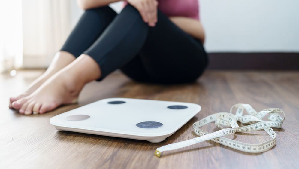 Pretila žena sjedi pored vage, ilustracija