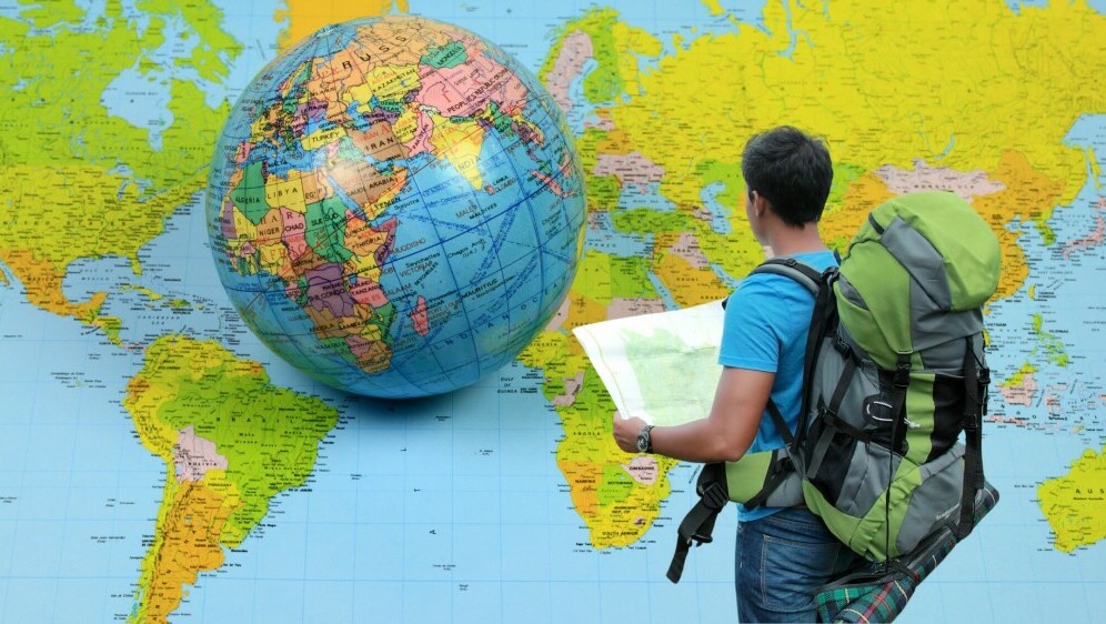 Muškarac s ruksakom i kartom ispred karte svijeta i globusa
