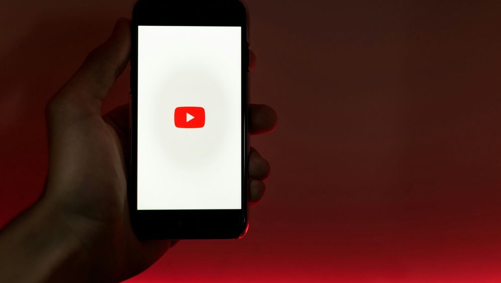 ruka koja drži mobitel s upaljenim zaslonom učitavanja youtubea