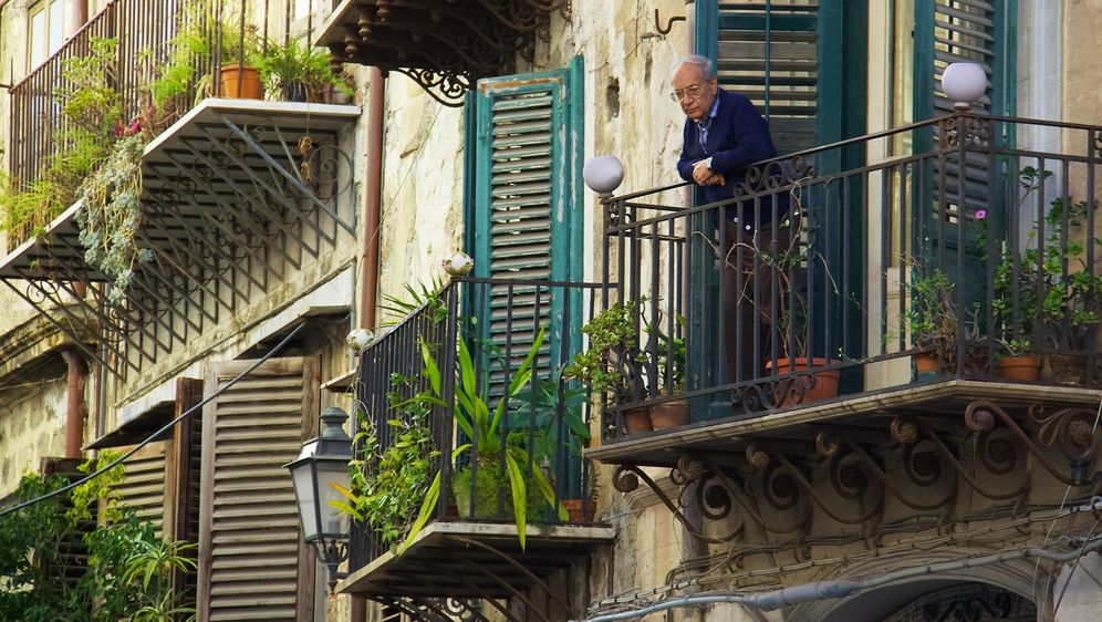 starac stoji na balkonu punom bilja