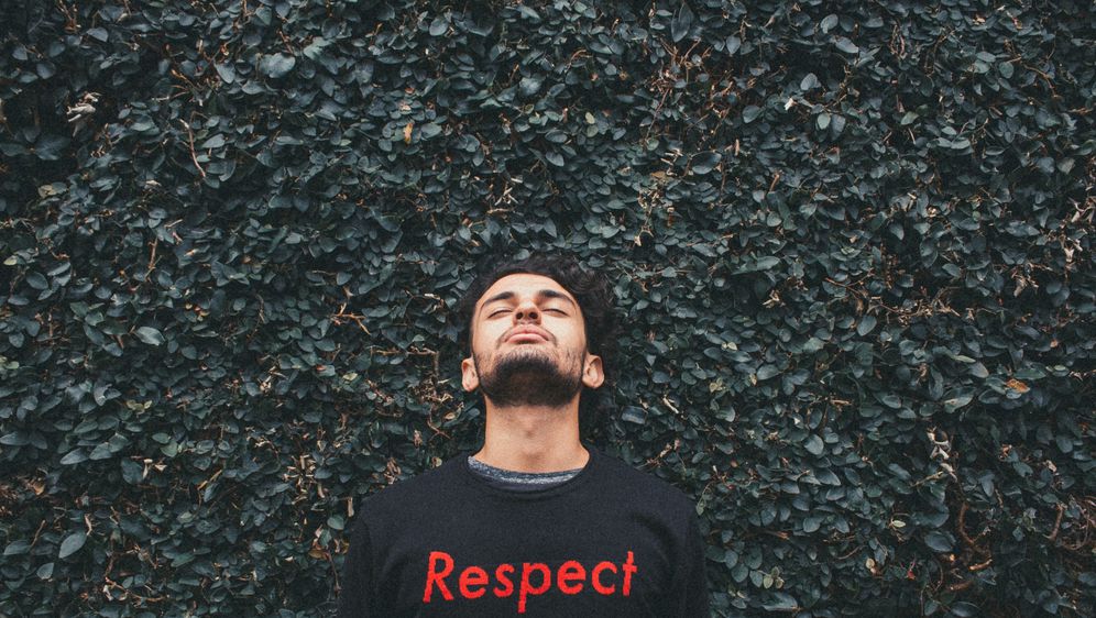 muškarac stoji ispred grmlja i gleda prema gore s majicom na kojoj piše respect