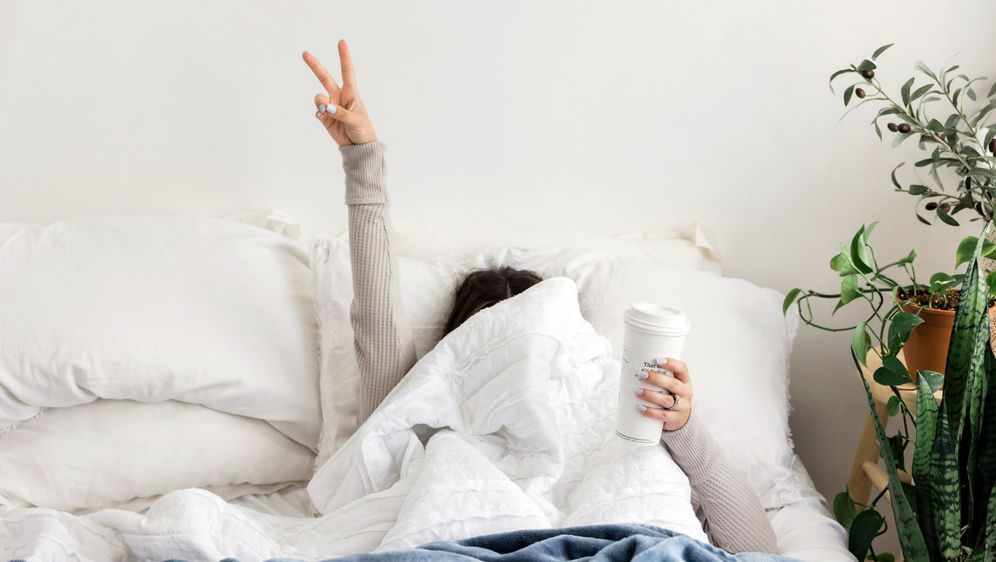žena u krevetu prekrivena preko glave drži dva prsta u zraku